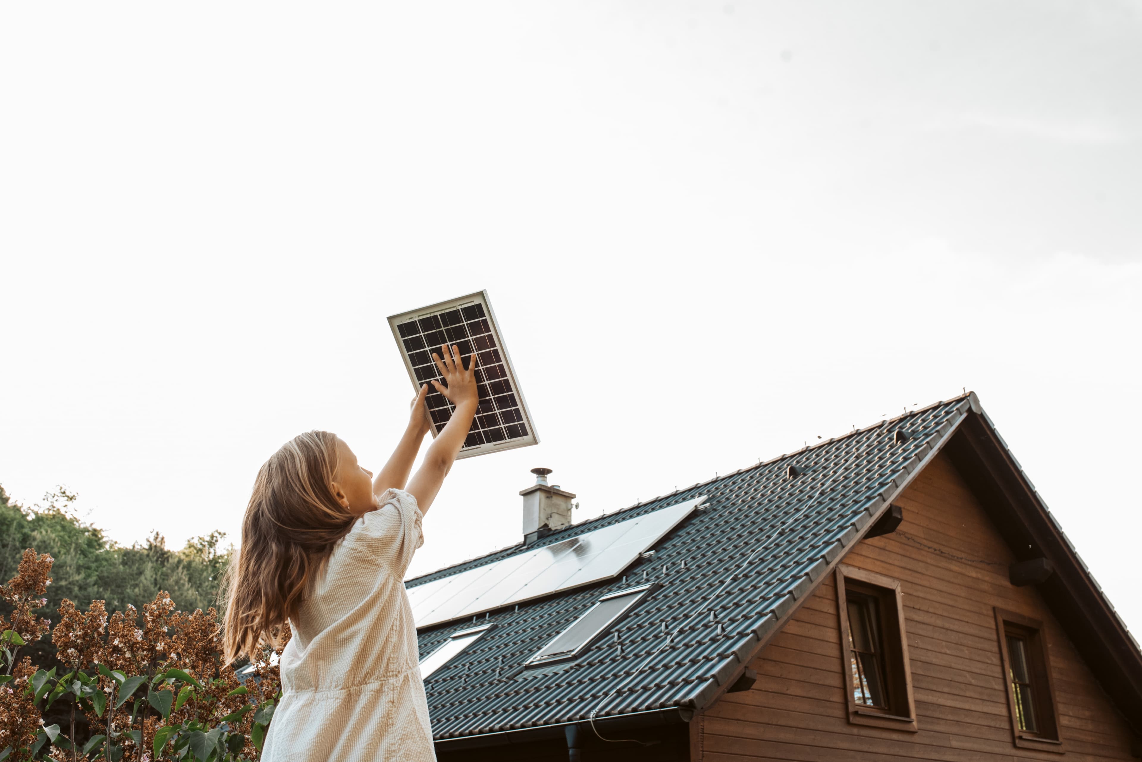 Mädchen hält Solarmodul vor Einfamilienhaus mit PV-Anlage